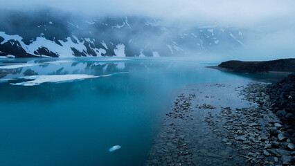 shot of the lake surrounded by mountains under the snow - capped mountain