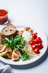 Breakfast plate with bread, tomatoes, cheese, arugula, nuts and figs on white background.