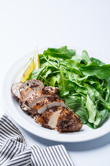 Green salad with grilled chicken breast on white plate, white background.