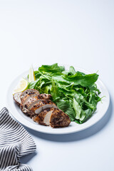 Green salad with grilled chicken breast on white plate, white background.