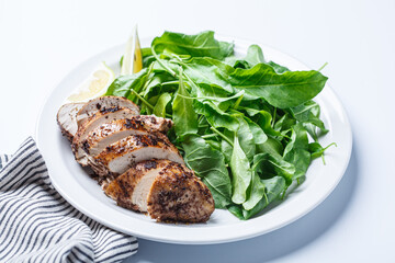 Green salad with grilled chicken breast on white plate, white background.