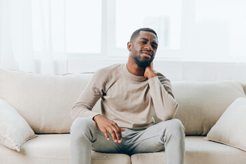 Tired African American Man with a Headache Resting on the Couch at Home Desperately Stressed and Depressed, Seeking Relief from Pain and Mental Health Issues Indoor Lifestyle Image