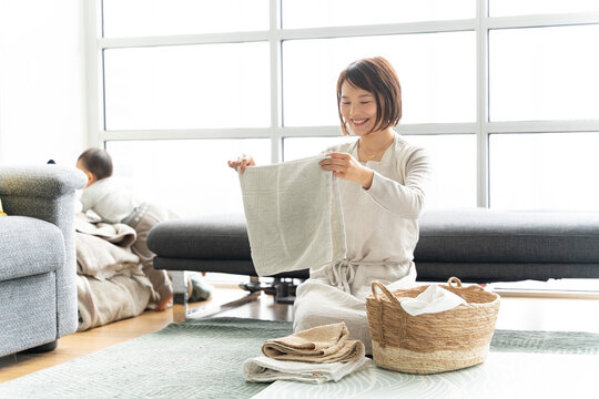 洗濯物を畳んでいる母親と部屋で遊んでいる赤ちゃん