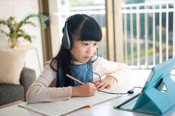 ヘッドフォンをして家のリビングで勉強をしている女の子