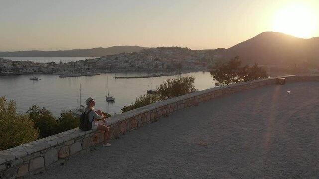 Enjoying vacation in Greece. Young traveling woman enjoying sunset on the view point. Ermioni bay and yacht marina.