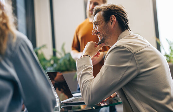 Business man smiling as he engages in a discussion with his colleagues in a meeting - Powered by Adobe