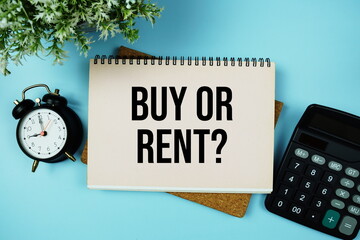Buy or Rent? text written on paper card with calculator and alarm clock on blue background