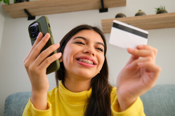 Latin female teenager with braces buying online in a smartphone with a credit card.