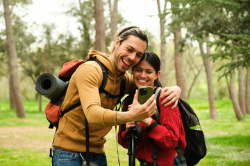 A man and a woman are smiling and taking a selfie in a park. They are using the smartphone