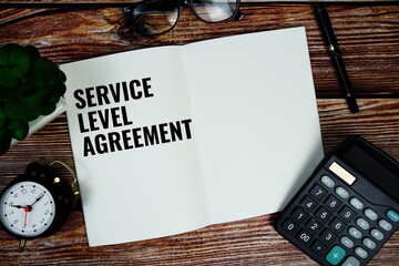 SLA (Service Level Agreement) text written on paper torn with calculaton and alarm on wooden background