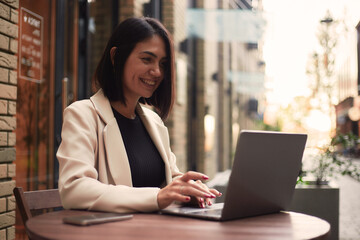 Young Asian business woman in a suit having breakfast in a cafe, working using a smartphone in a cafe. Happy smiling professional woman working with laptop young businesswoman in suit