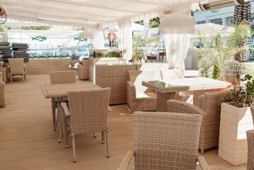 Wicker furniture tables in the open air are waiting for visitors. The interior of the restaurant in the open air. Empty tables of street cafe.