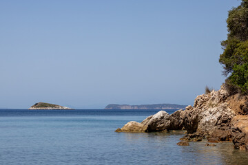 Fototapeta premium Panoramic view of a serene coastal landscape featuring calm blue waters and distant hills under a clear sky. Peaceful and tranquil scene perfect for relaxation and travel concepts.