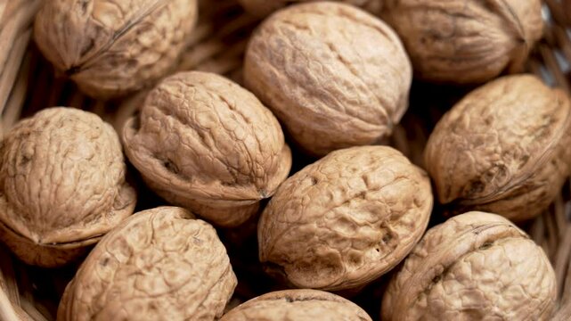 Full rattan rustic bowl filled with whole rough walnuts. Intricate nut shell texture. Protein and fiber from plant sources. Rotation. Top view