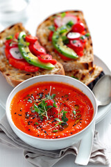 A bowl of soup with a spoon and a plate of bread with avocado and tomatoes. Scene is healthy and inviting