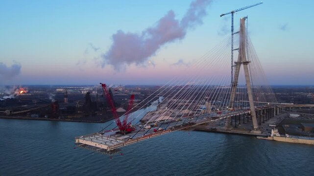 Construction of the Gordie Howe International Bridge at Sunset with steel mill on Zug Island in background