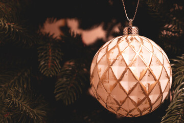 White Christmas bauble with golden glitter hanging on a fir tree. Place for text.