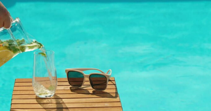 A refreshing glass of lemonade being poured next to sunglasses by the pool.