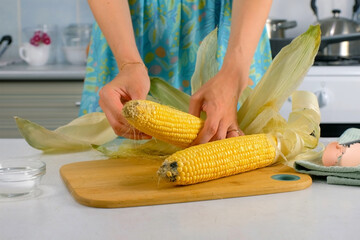 Woman peeling ears of corn removing leaves on wooden board cooking on kitchen at home. Cuisine culinary prepare cook dish domestic food recipe ingredients. Healthy nutrition eating vegetables.