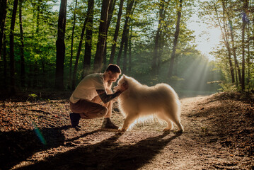 millennial hipster male with tattooed arms walking and playing with his cute and fluffy samoyed dog...