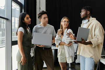 A group of young entrepreneurs brainstorm ideas, laptops in hand, in a modern office setting.