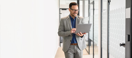 Portrait of happy young male professional working on project over wireless computer in office...