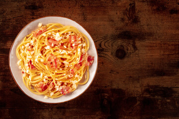 Carbonara pasta dish, traditional spaghetti with pancetta and cheese, overhead flat lay shot with copy space, on a wooden table
