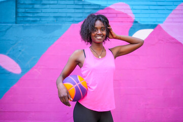 Portrait of a cheerful african basketball player against urban wall