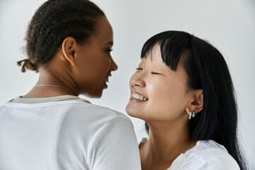 Obraz premium Two young women, lesbian couple, share a tender moment together against a gray backdrop.