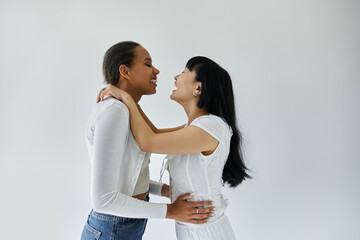 An interracial lesbian couple shares a tender moment, their laughter echoing in the quiet studio.