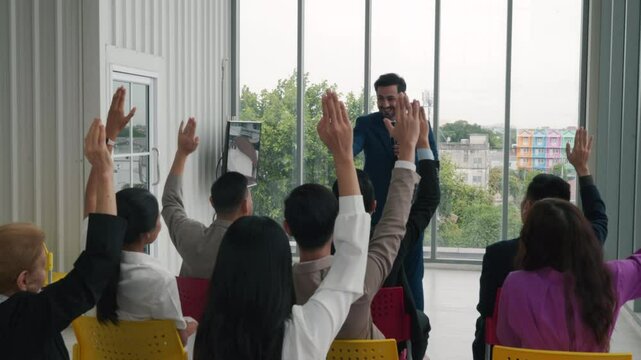 At a corporate event, a diverse audience of businesspeople raises their hands for questions, voting, or volunteering. The scene highlights teamwork and interactive audience participation.