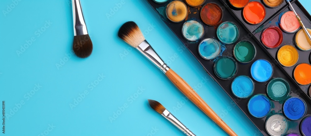 Poster close up of watercolor paints and brushes on a blue background with copy space image available