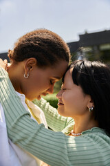 Two young women, one African American and one Asian, embrace, their foreheads touching in a loving gesture.