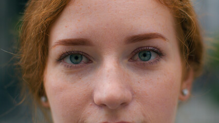 Close up beautiful smiling young Caucasian ginger woman face female lady girl slowly wide opening bright blue eyes looking camera outside city urban street. Clear vision makeup eyesight ophthalmology