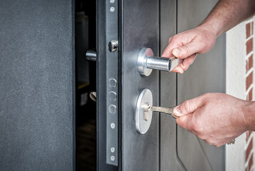 Hand putting house key into front door lock of house