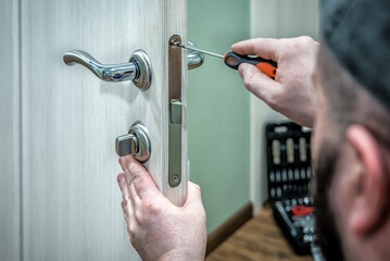 Professional locksmith worker installing the part of lock in wooden door by the screwdriver
