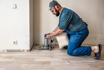 Professional worker with orbital sander for grinding parquet floor in difficult place. Industrial theme