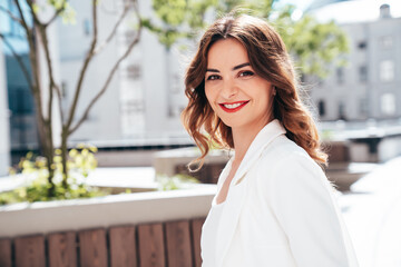 Young beautiful brunette woman wearing nice trendy white suit jacket. Sexy smiling model posing in the street at sunny day. Fashionable female outdoors. Cheerful and happy. Evening makeup, red lips