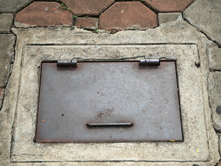 Medium-sized manhole cover, old condition, rusted, on the sidewalk.