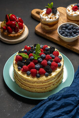 Homemade cake with fresh berries and sweet desserts on dark background.