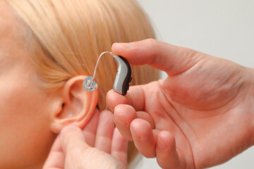 Fototapeta premium Doctor putting an hearing aid. The hands of a male audiologist trying on a hearing aid on a woman's ear. Helping technologies for people with disabilities
