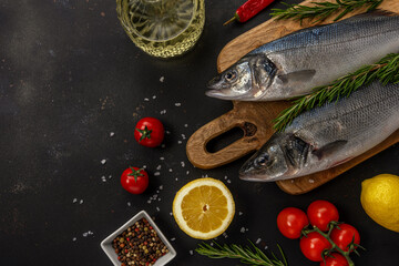 Two fresh seabass fishes with rosemary and vegetables on black table. Seafood concept.