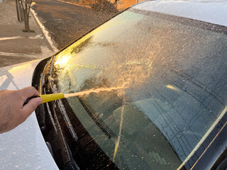 A person washes the windshield of a car with a hose.