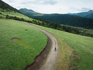 Fototapeta premium Aerial view of woman riding mountain bike on flowering grassland mountain