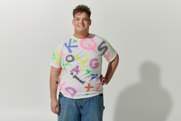 Fototapeta premium Short, dark-haired queer person in white tee and blue jeans by white wall