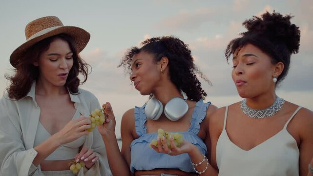 Three women eating grapes and laughing on jokes outdoors