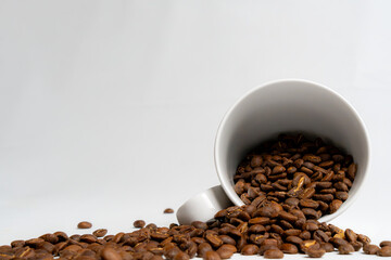 arabica roasted coffee bean's spill from a white mug, isolated on white background