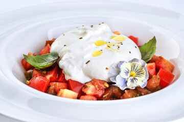 Burrata cheese with tomatoes, edible flower and basil, on a plate on a white background.