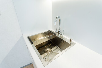 In this kitchen, there is a sturdy stainless steel sink with a matching faucet, enhancing its contemporary look. The fixtures are crafted for practicality and visual appeal