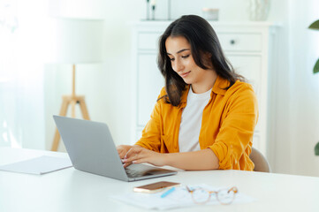 Focused successful pretty arabian or indian ethnicity young woman in an orange shirt, IT...